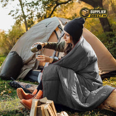 PrepPro Australia grey wearable quilted camping blanket draped over a woman sitting by a tent in the woods