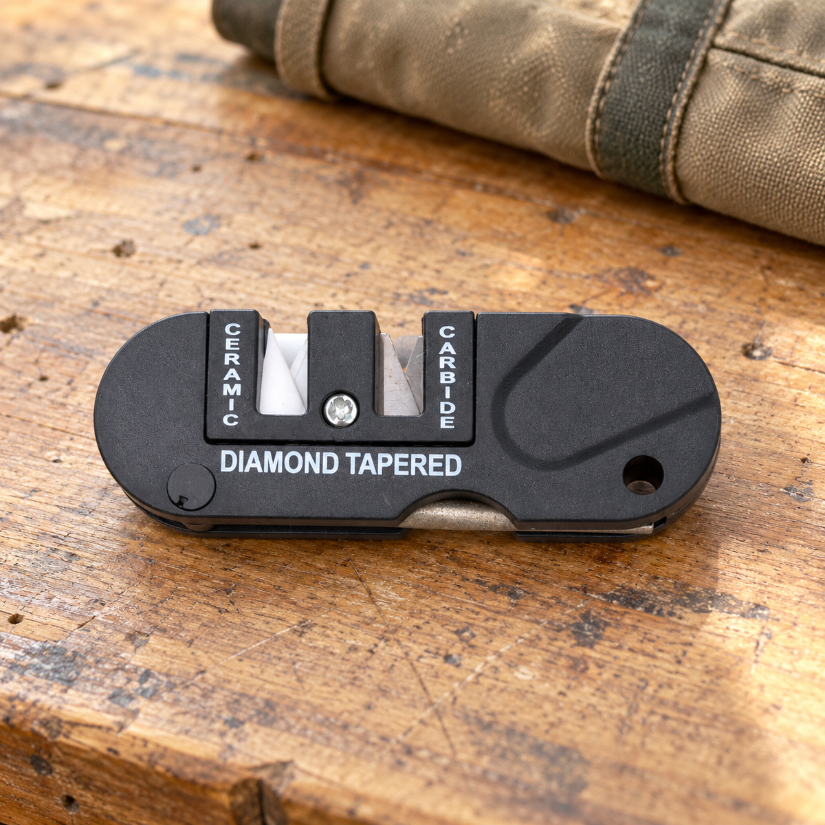 Black pocket knife sharpener with folded diamond rod on a wooden workbench